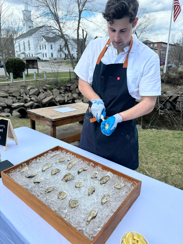 a person in an apron is preparing oysters on ice