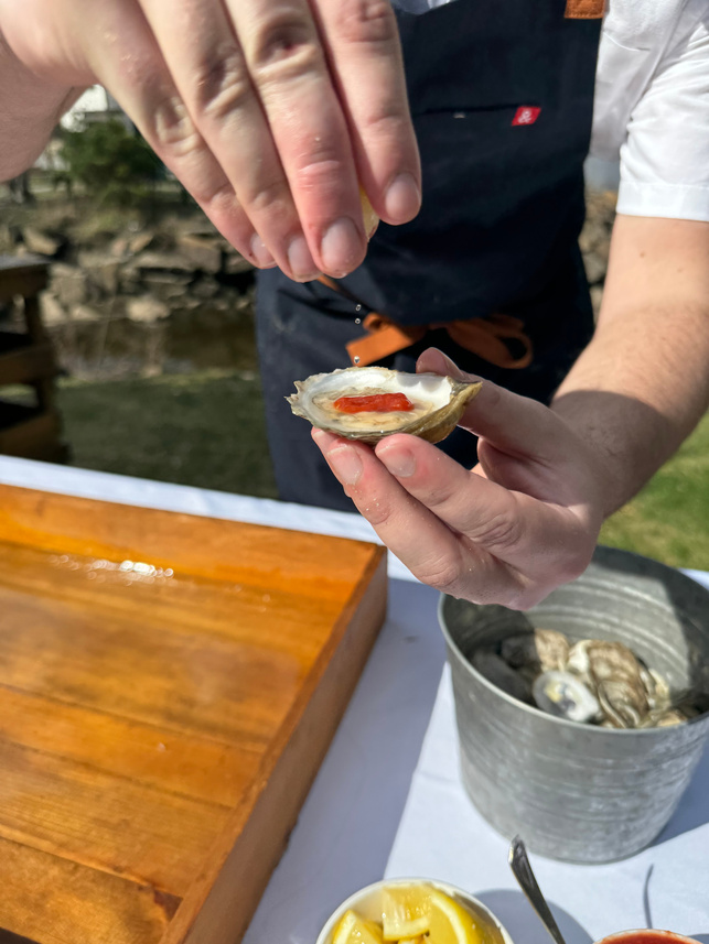 a person in an apron is holding an oyster on a wooden cutting board